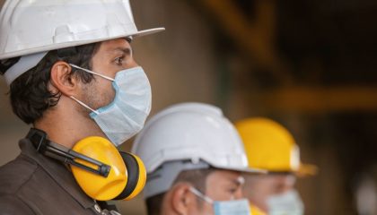 comstruction worker men wearing protective gear and surgical masks standing in line